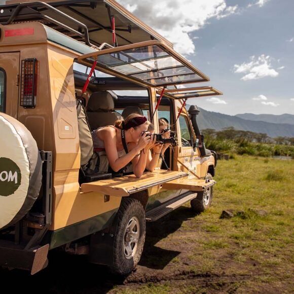 Personen im Tanzania Specialist Jeep auf grünem Gras machen Bilder, Berge im Hintergrund