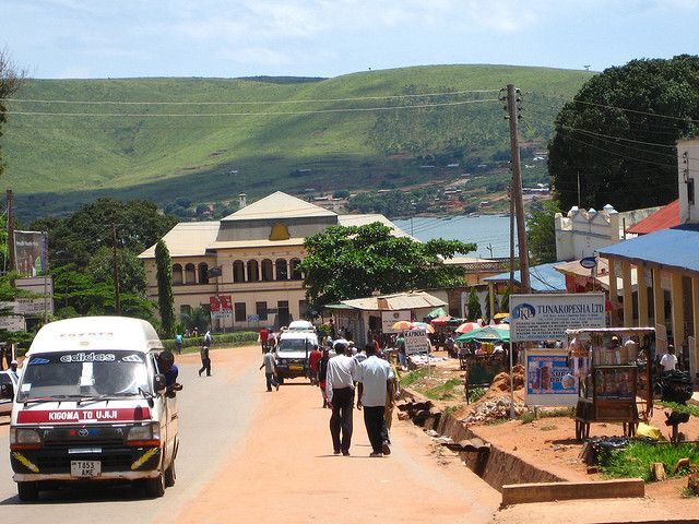 Straße mit Auto und Menschen, grüner Hügel und Gebäude im Hintergrund